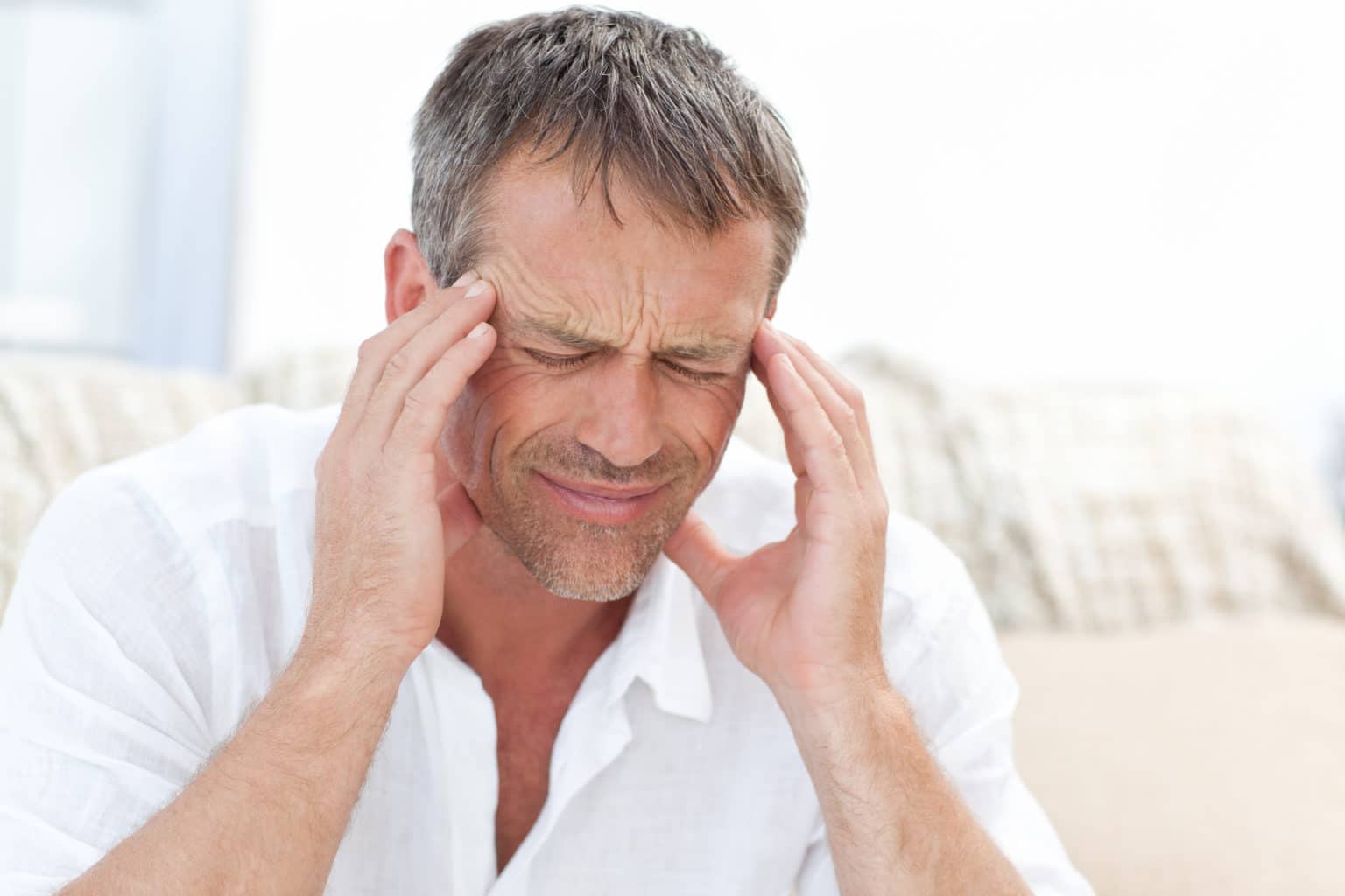 Person holding both temples with a pained facial expression while experiencing facial discomfort.